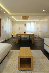 moderner luxuriöser Wohnbereich mit Eichenholztisch und edlen weiß lackierten Schränken, Decke mit indirekter Beleuchtung