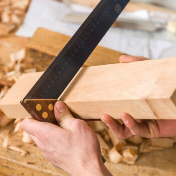 2 Hände halten ein Massivholz, mit einem Winkel wird die Arbeit geprüft